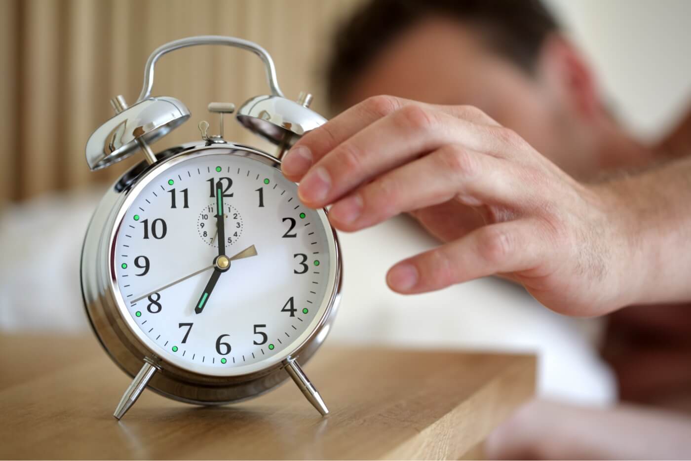Night Shoot Survival Guide Man lying in bed turning off an alarm clock in the morning at am