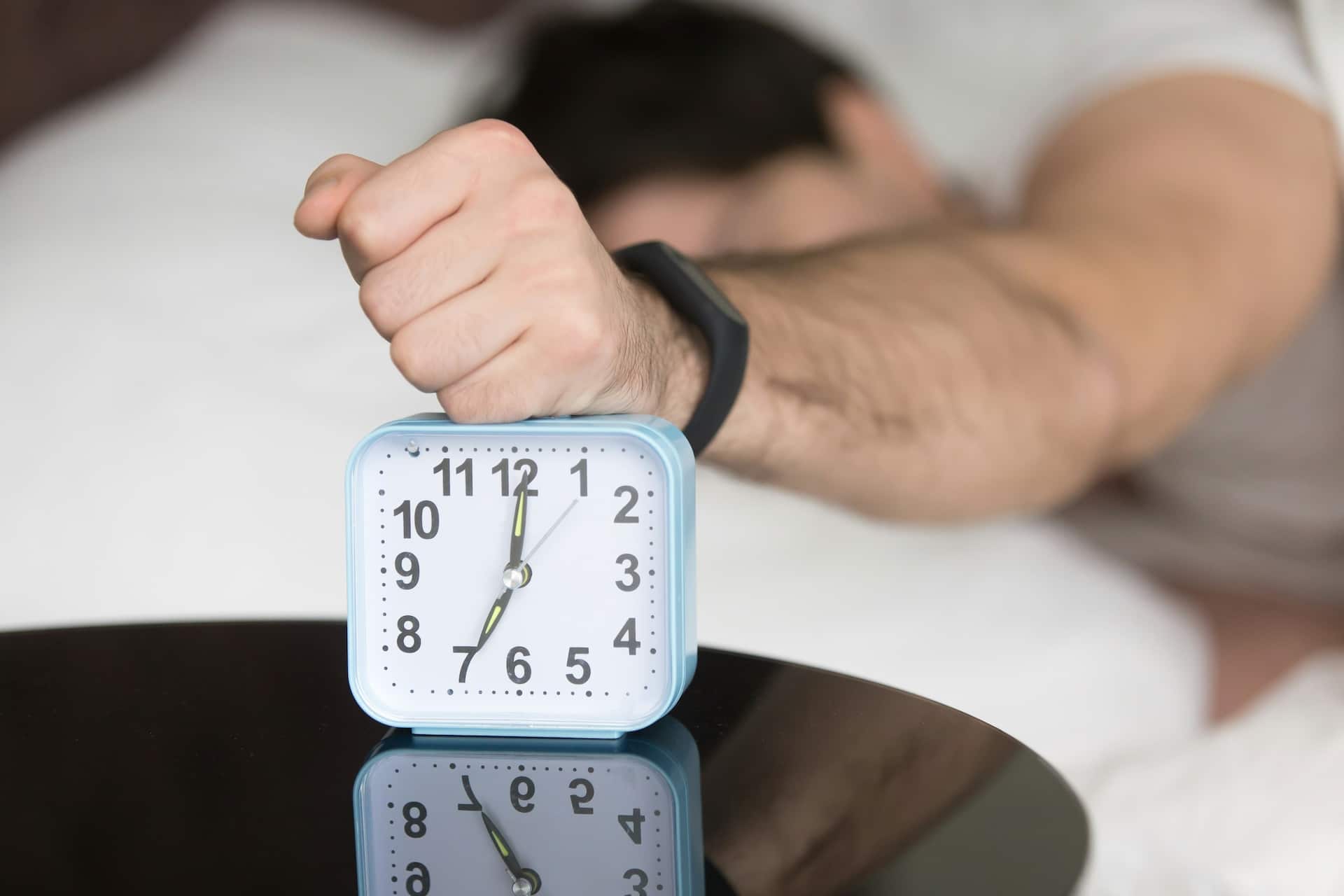 Night Shoot Survival Guide Man lying in bed turning off an alarm clock in the morning at am